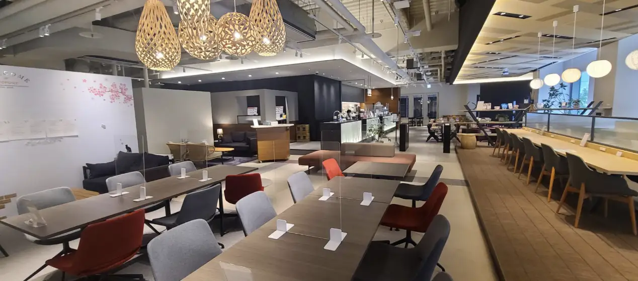 A spacious indoor room featuring several tables and chairs arranged neatly. The walls are adorned with a simple design, and there is a ceiling fixture above. The floor is well-maintained, contributing to the overall ambiance of the space.