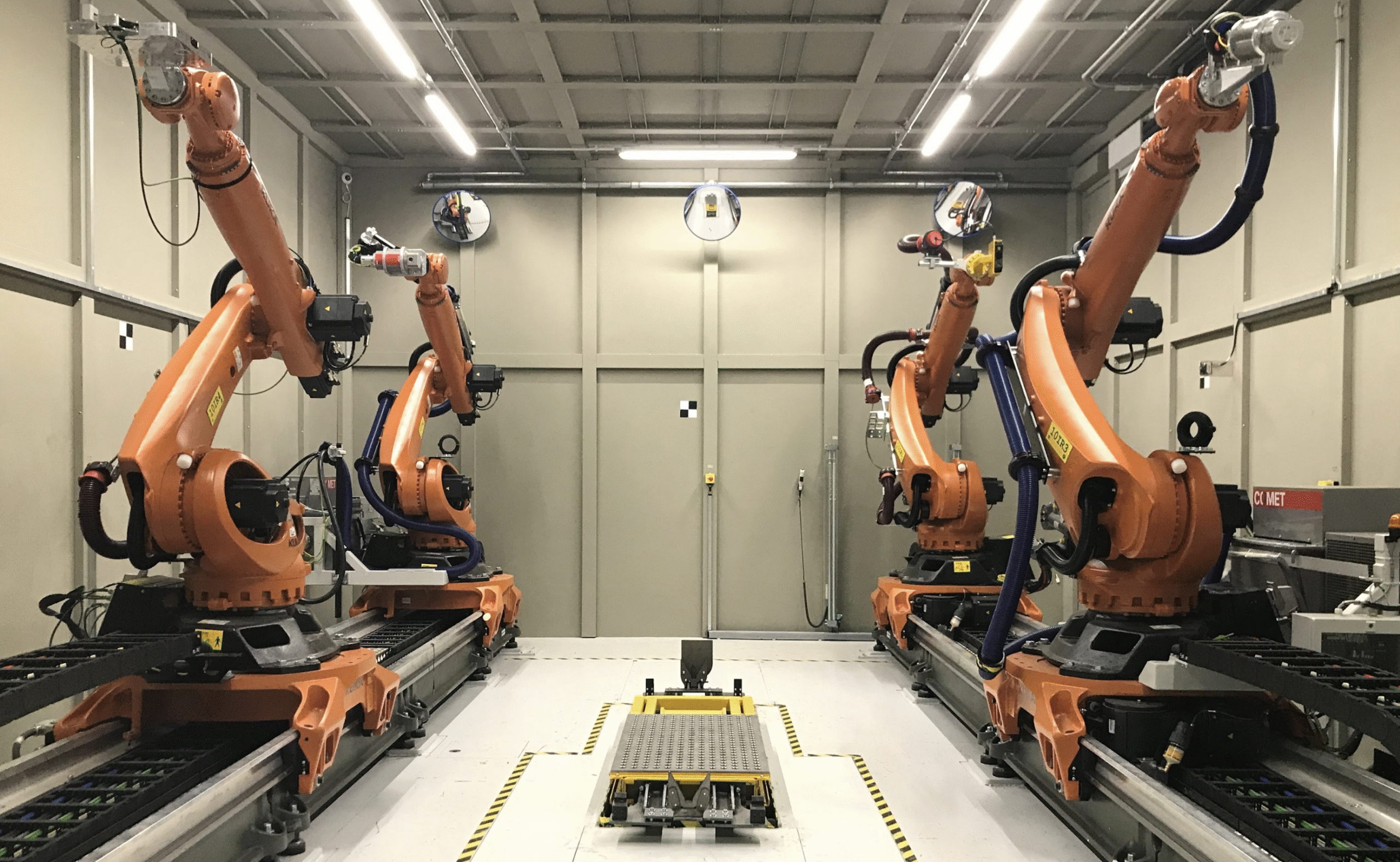 Robots operate on a factory floor, working alongside a conveyor belt transporting products