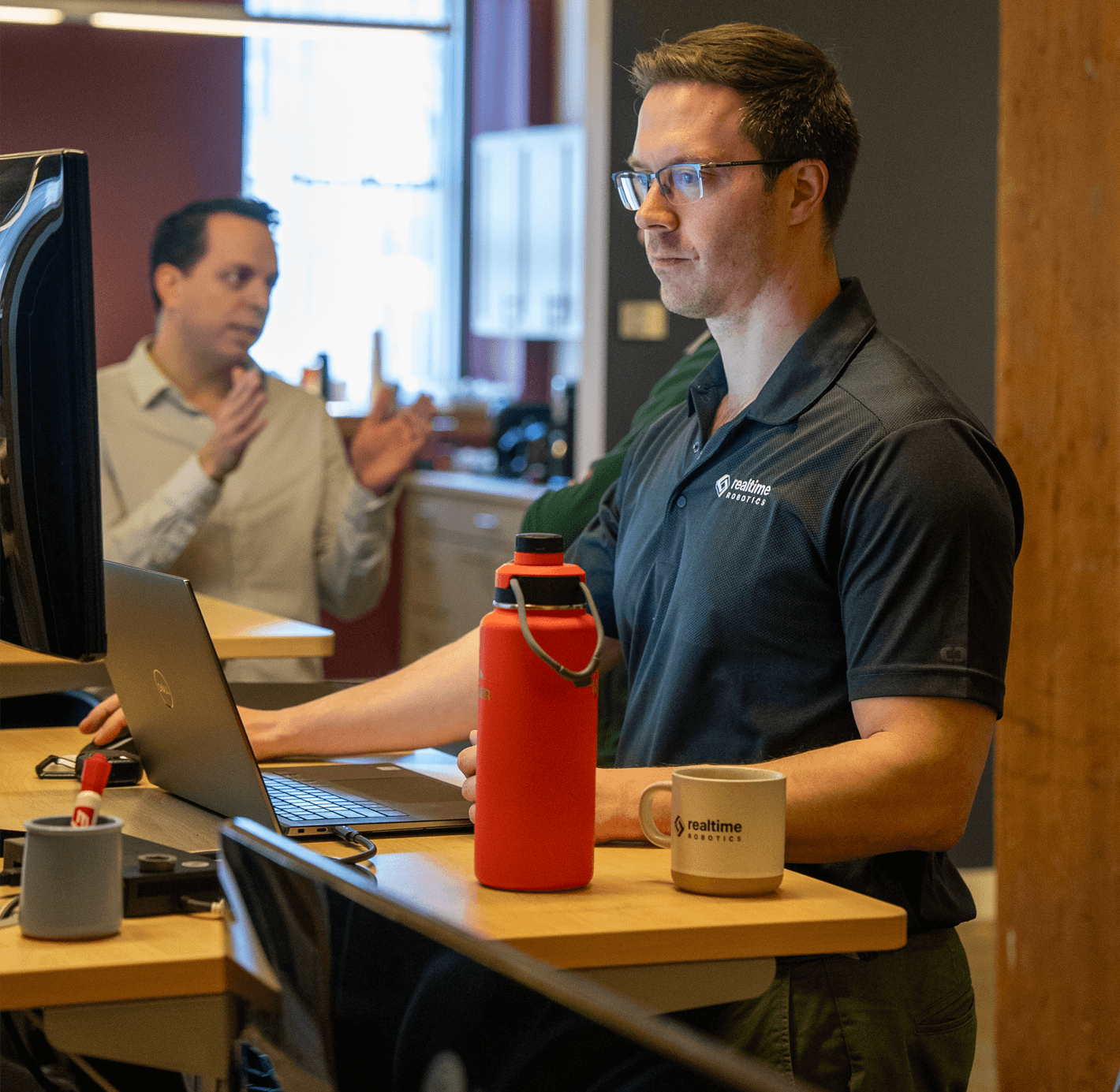 Team member wearing a Realtime Robotics polo shirt with a Realtime Robotics coffee mug on his desk